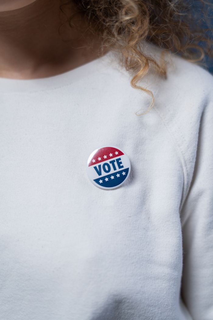 A close-up of a voter wearing a vote button on a white sweater, symbolizing civic duty.